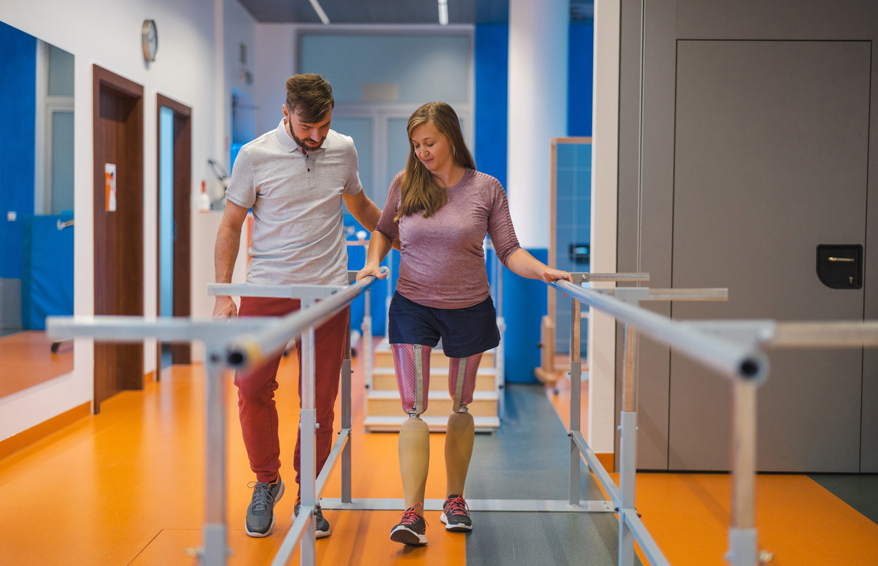 Young woman walking with prosthetic limbs being assisted by male physiotherapist